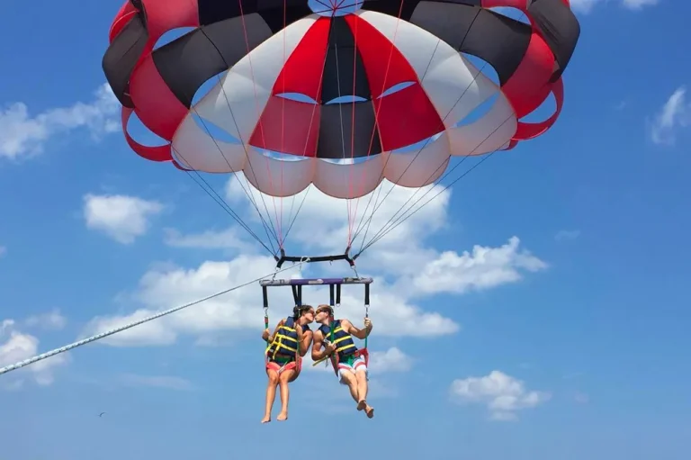 Riders soaring under a colorful parasail against a blue sky in Nags Head