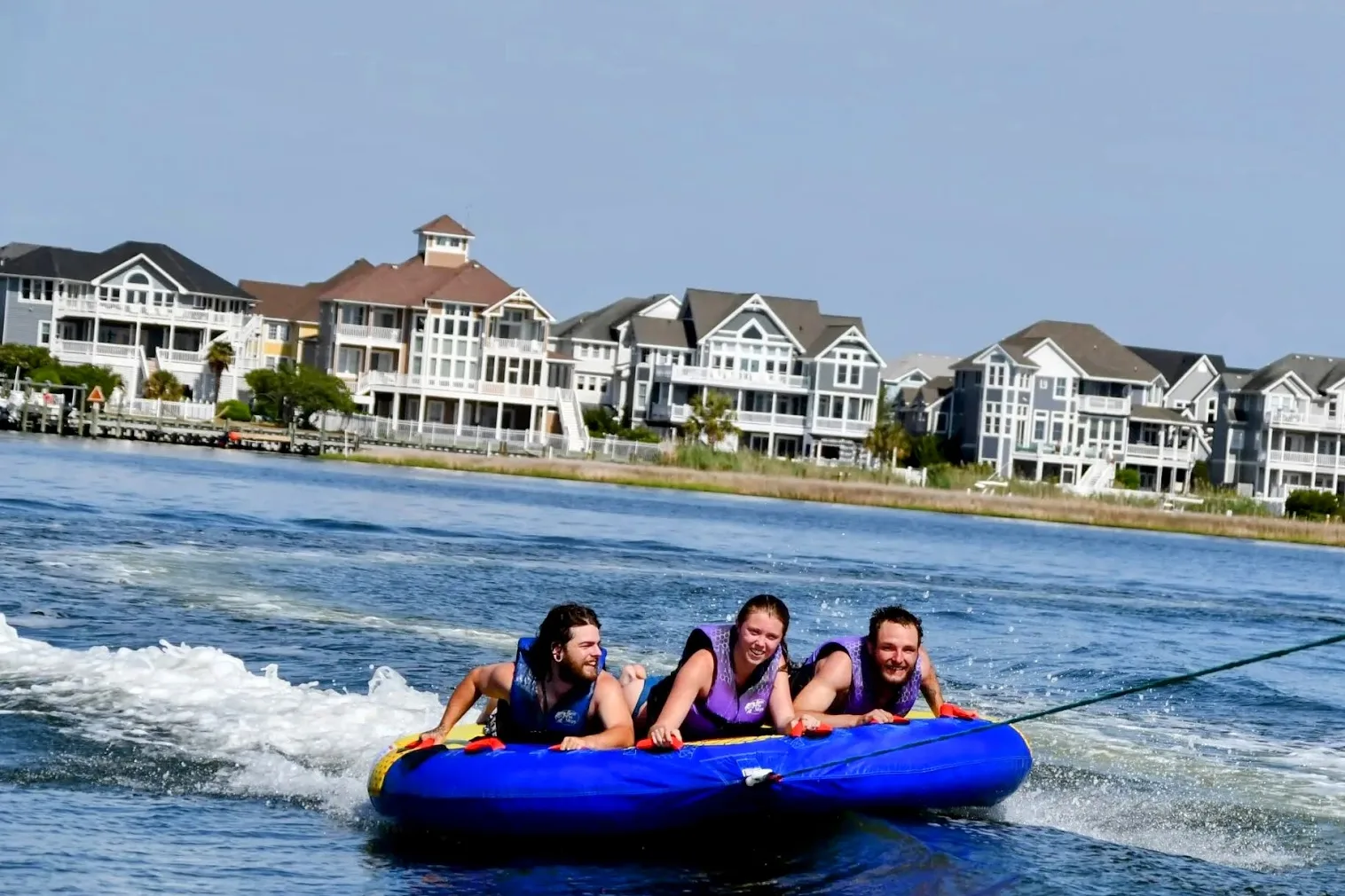 Three tubers riding behind the boat with Outer Banks beach houses in the background