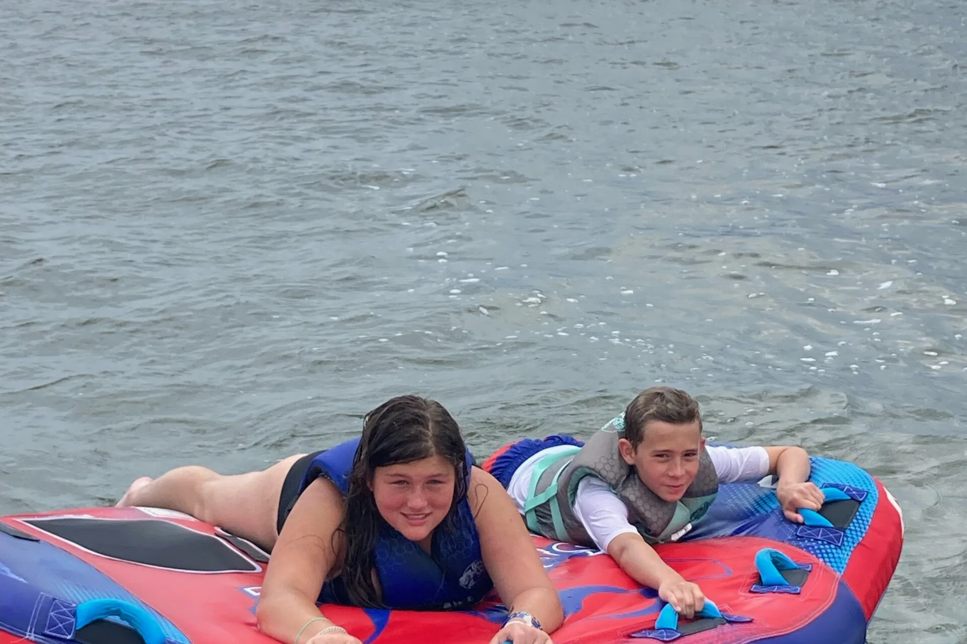 Two kids riding a red towable tube in Nags Head