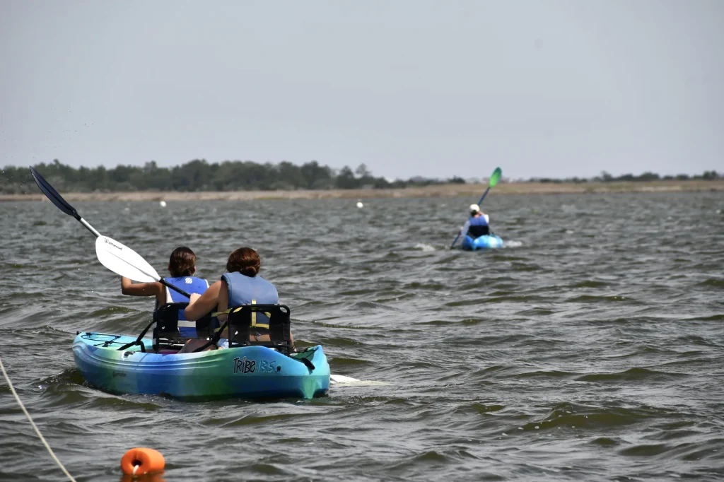 Guests paddling tandem kayaks toward the marsh