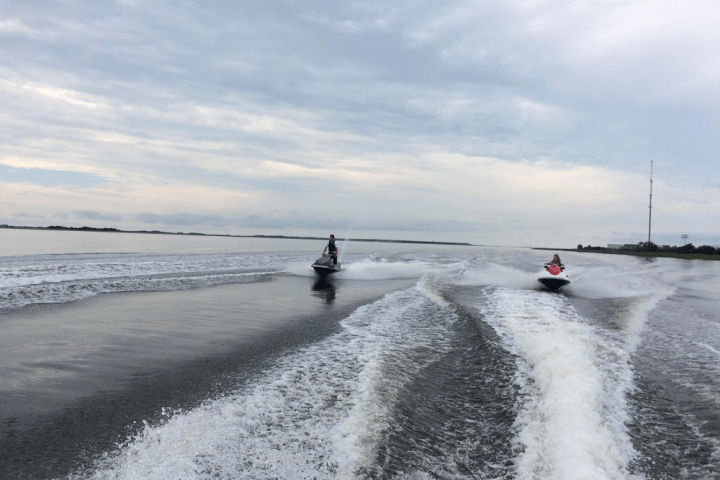 A couple of people racing on a jet ski rental ion the calm waters of Nags Head.