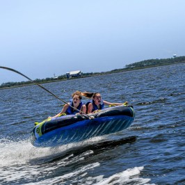 Two girls try to hang on during their exciting tubing trip in Nags Head, with Causeway Watersports.