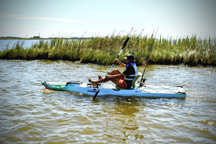 Man kayaking on a lake with tall grass and blue sky in the background.