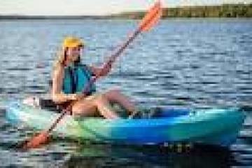 Person kayaking on a lake wearing a yellow cap and life vest.